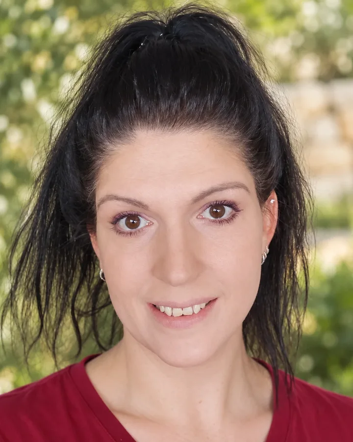 Monika Uebele, Gründerin von Soulfire Rebellion, lächelnd mit hohem Zopf vor grünem Garten. Echtes Foto, Hintergrund mit KI verändert.